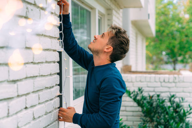 A man hangs decorative lights on a brick wall, showcasing Night Vision Lighting & Electric's installation services.