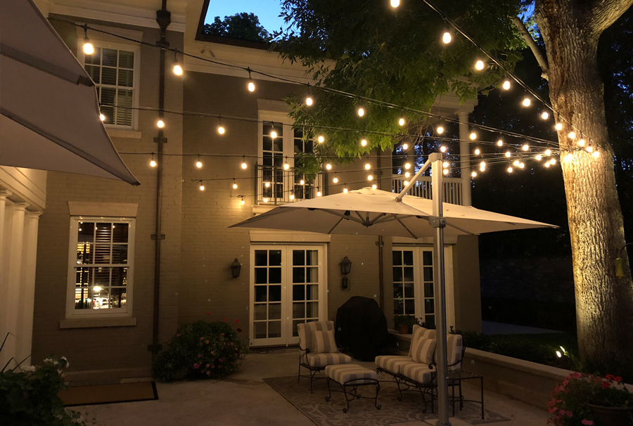 Outdoor patio illuminated with string lights, showcasing Night Vision Lighting & Electric's elegant lighting design.<br />