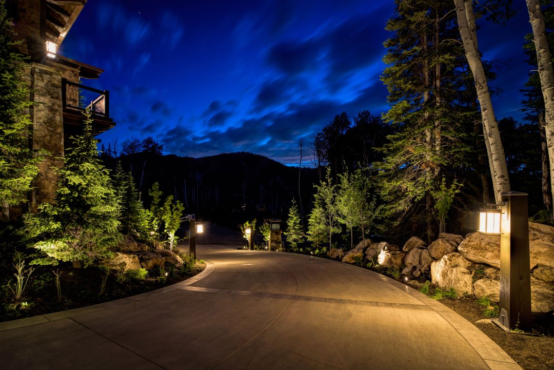 Nighttime view of a driveway with glowing trees and lights, highlighting the work of Night Vision Lighting & Electric.